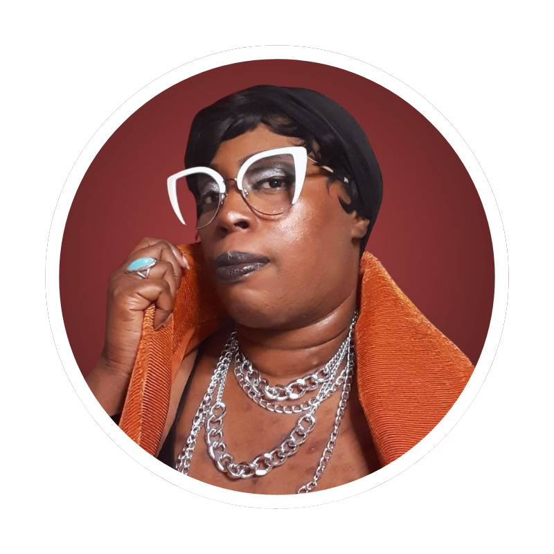 Avatar (Me) Georgina Kiersten -1 Photo of Georgina Kiersten (Jasper Hyde) - a photo of a Black feminine trans masculine non-binary p;erson in a short black wig, big white oversized glasses, and a orange jacket.