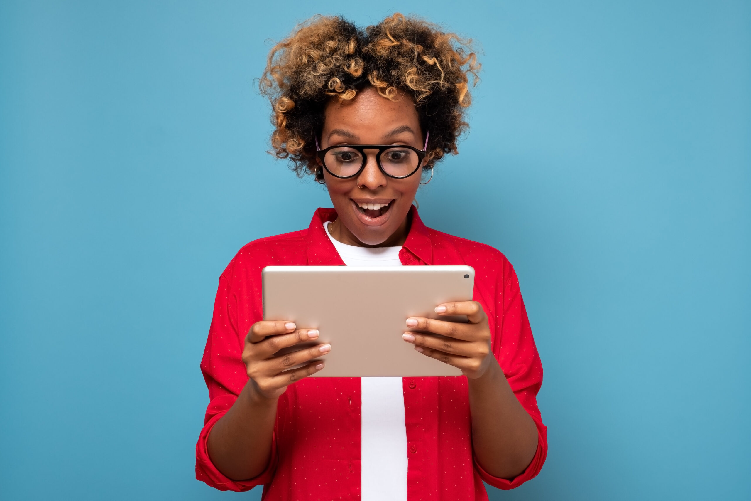 a Black woman wearing glasses looking a tablet in shock. 